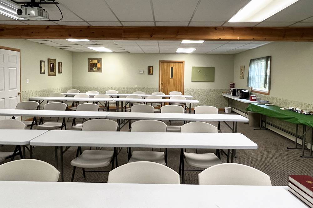A meeting room with long white tables and folding chairs, and two red Bibles on a table in the foreground.