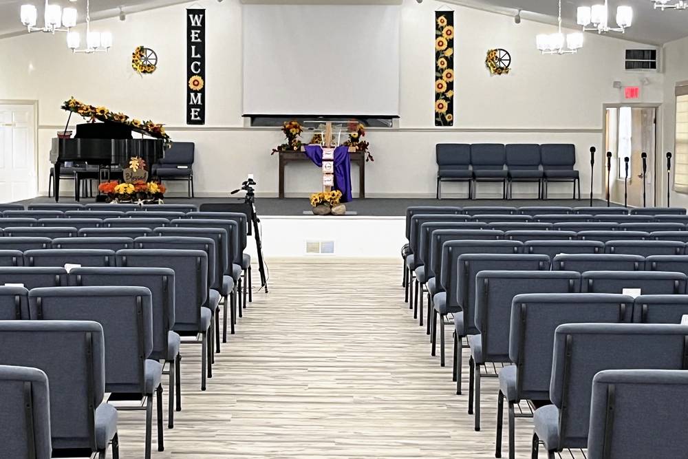 The sanctuary seen from the back: rows of gray padded chairs on both sides of a center aisle, with a piano, a screen, and welcome banners at the front.
